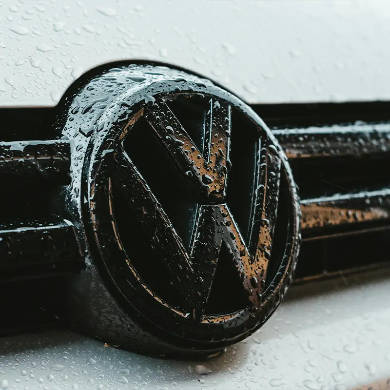 Detalle del logotipo Volkswagen en coche de importación alemana con gotas de lluvia.
